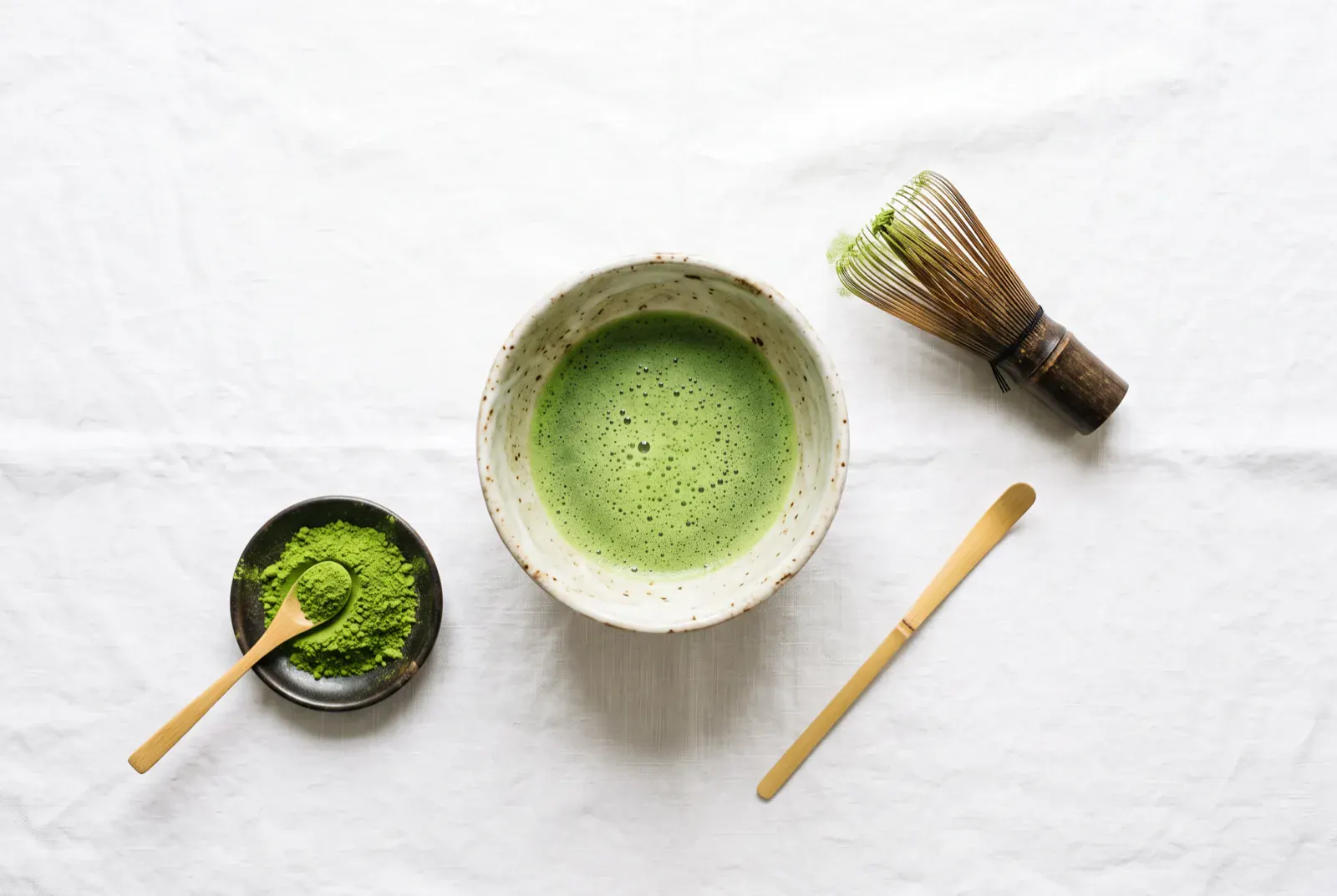 Bol chawan de matcha fouetté, fouet chasen, cuillère chashaku et matcha en poudre sur lin blanc